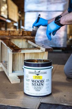 a man in blue gloves is using a paint can to finish a piece of wood