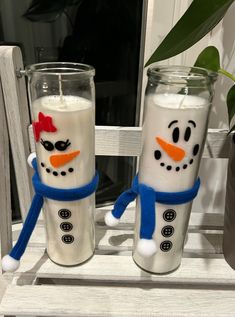 two frosty snowman candles sitting next to each other in front of a window