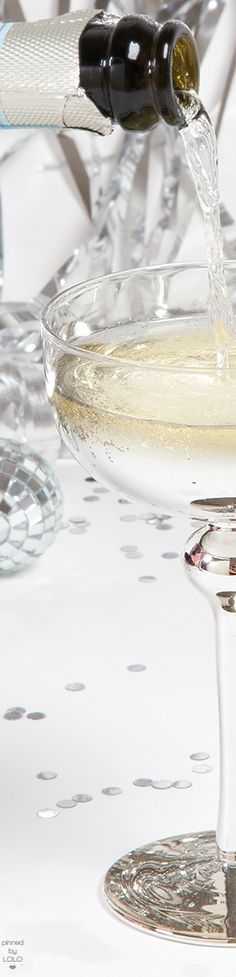 champagne being poured into a wine glass in front of other glasses on a white table