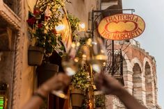 two people toasting with wine glasses in front of a building that has an italian restaurant on it