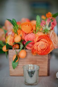 an arrangement of orange flowers and greenery in a wooden vase on top of a table