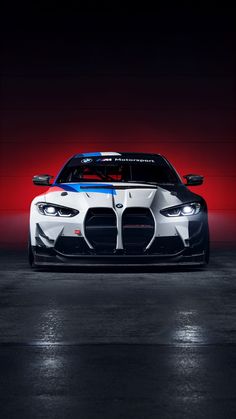 the front end of a white and blue sports car in a dark room with red lighting