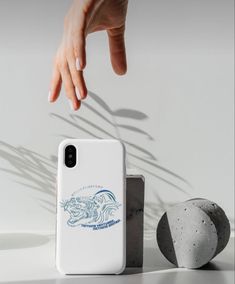 a hand reaching for something on the ground next to a white phone case and rock