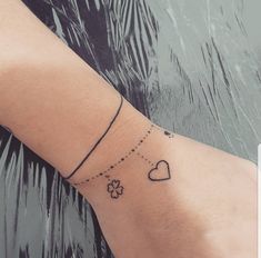 a woman's arm with a small tattoo on the wrist that has hearts and clovers attached to it