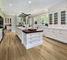 a large kitchen with white cabinets and wood flooring in the center is featured on this page