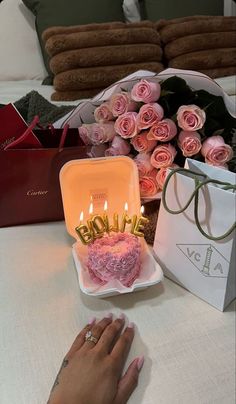 a woman's hand next to a pink heart shaped cake with candles on it