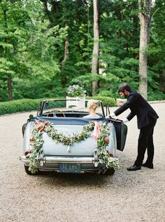 a bride and groom standing next to an old car decorated with greenery for their wedding