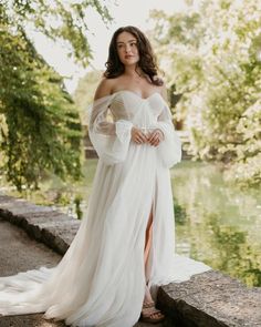 a woman in a white dress standing on the edge of a river with her hands on her hips