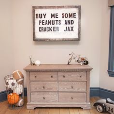 a wooden dresser sitting on top of a hard wood floor next to a framed sign