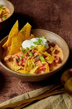 two bowls filled with nachos and tortilla chips on a brown table