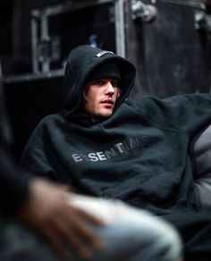 a man in a black hoodie sitting on a couch with his arm wrapped around him