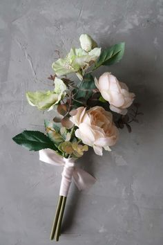 a bouquet of flowers with green leaves on a gray surface, ready to be used as a boutonniere