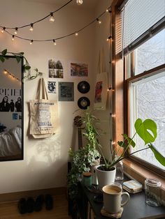 a room filled with plants and pictures on the wall next to a window covered in string lights