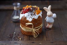 a cake with white frosting and fruit on top, next to a small bunny figurine