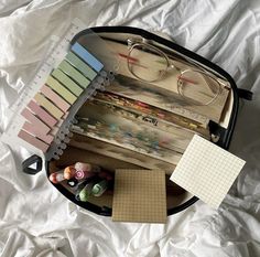 an open suitcase filled with lots of crafting supplies on top of a white sheet