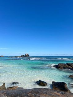 the ocean with rocks and clear water under a blue sky