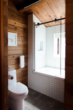 a bathroom with wood paneling and a white toilet next to a window in the corner