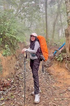 a woman with a backpack and hiking poles on a trail in the woods, smiling at the camera