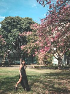 a woman is standing in the grass by some trees