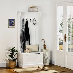 a white coat rack with clothes hanging on it and two plants in the corner next to it