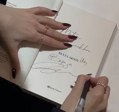 a woman is writing on a book while holding a pen in her hand and wearing gold rings