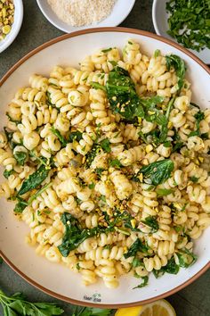 pasta with spinach and parsley in a white bowl next to lemons, garlic, and other ingredients