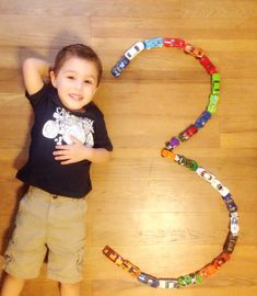 a young boy standing in front of the number 3 made out of legos on a wooden floor