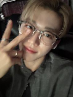 a young man wearing glasses making the peace sign with his hand while sitting in a car