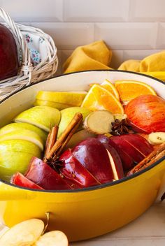 apples and oranges in a yellow bowl on a counter next to other fruit items