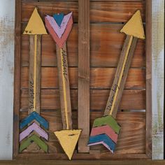 three wooden arrows with writing on them in front of a wood box that is painted yellow, purple, and green