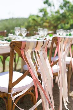 the chairs are lined up with ribbons and wine glasses on top of each chair for an outdoor wedding reception