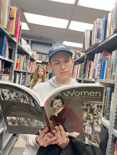 a young man reading a book in a library with other people behind him and shelves full of books