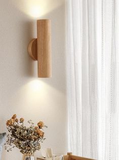 a vase with flowers sitting on a table next to a wall mounted lamp and window