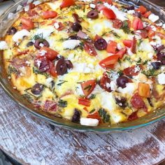 a pizza with olives, tomatoes and cheese in a glass dish on a wooden table