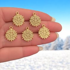 small gold snowflake charms in the palm of someone's hand