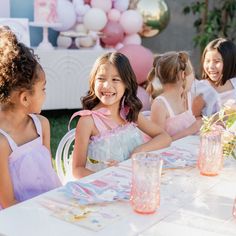 three girls in pink dresses are standing near a table with balloons and cake on it