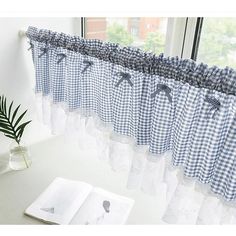 blue and white checkered curtains hanging in front of a window with an open book