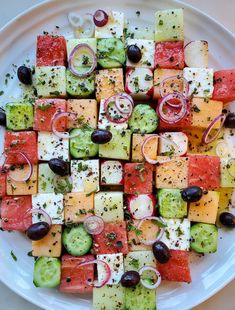 a white plate topped with cucumbers, tomatoes and olives next to other vegetables