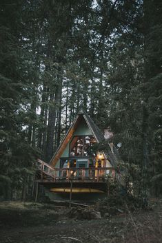 a small cabin in the woods with people sitting on it's porch and looking out at the trees