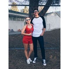 two people standing next to each other in front of a chain link fence and tree