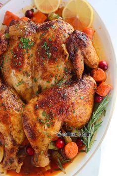 a white plate topped with chicken, carrots and cranberries next to lemon wedges