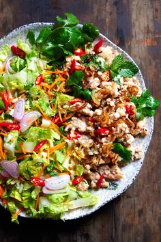 a salad with chicken and lettuce is on a white plate next to a wooden table