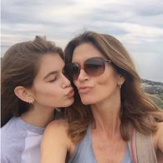 two women kissing each other while standing on top of a hill in front of the ocean