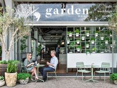 two people sitting at tables in front of a garden shop