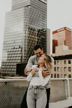 a man and woman standing next to each other in front of tall buildings with their arms around each other