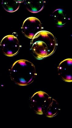 soap bubbles floating in the dark with colored lights on them's sides and black background