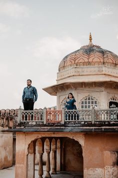 a man and woman standing on the balcony of an old building looking at something in the distance