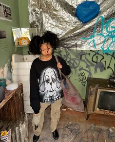 a woman standing in a room with graffiti on the walls and holding a plastic bag