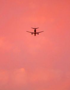 an airplane is flying in the pink sky