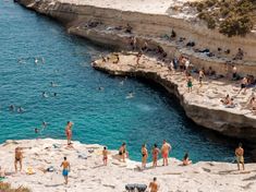 many people are swimming in the water near some cliffs and beach chairs on the shore